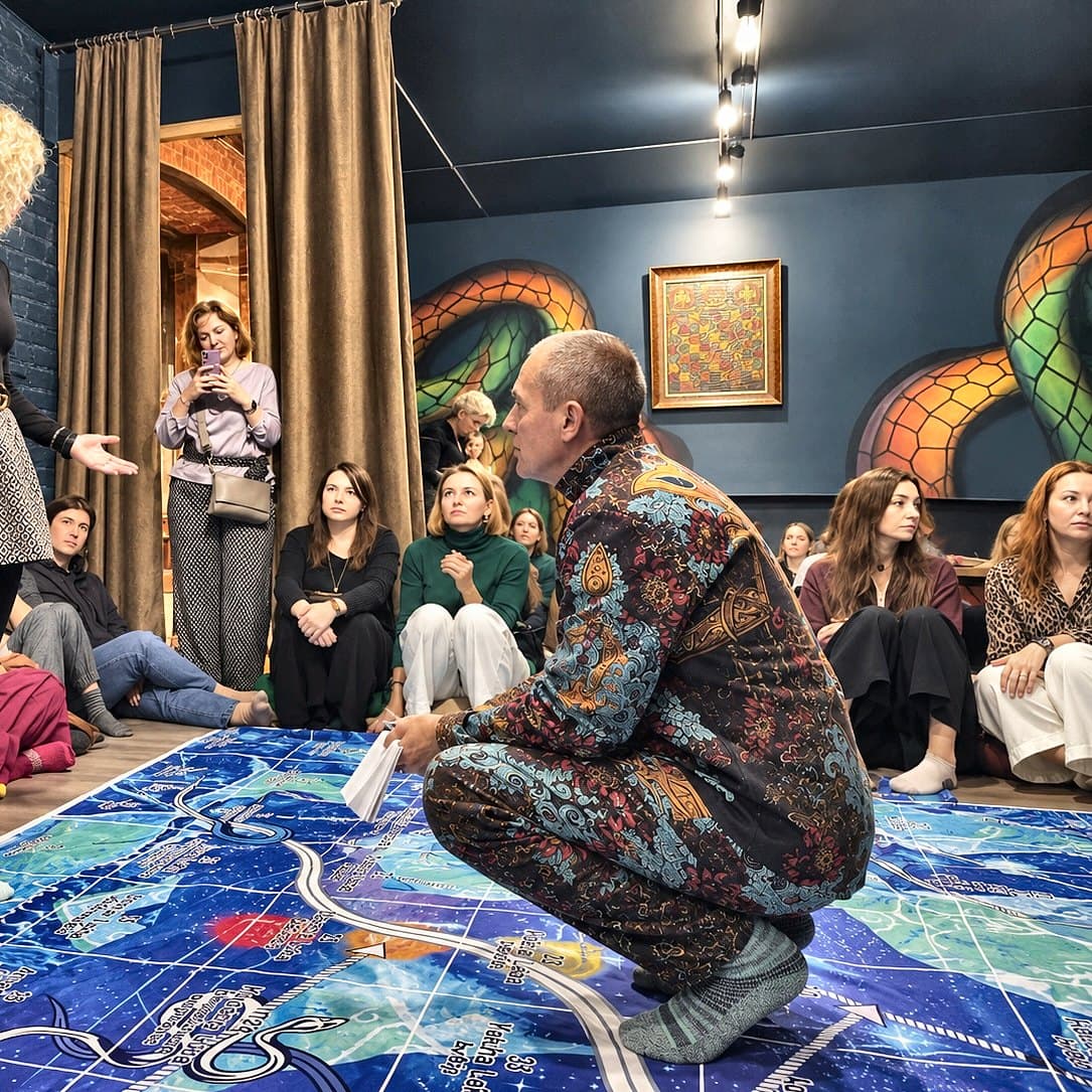 A group session of Leela: the teacher crouched over a full-size floor board, students seated around it